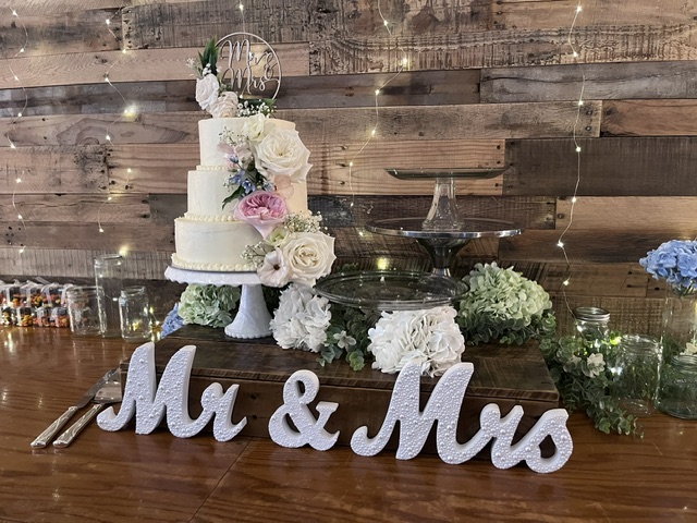 Wide reception table view of tiered wedding cake and glass dessert stands